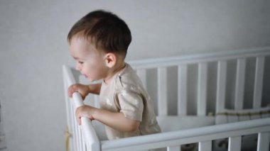 Beyaz beşiğinde gülümseyen beyaz çocuk. Neşeli çocuk mutlu bir şekilde zıplar ve etrafa bakar..