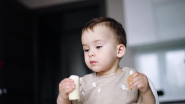 Küçük çocuk iki elinde de yemek tutuyor. Tatlı bebek muz yiyor. Düşük açı görünümü.