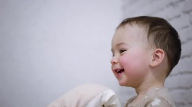 Sevimli pembe yanaklı, gülümseyen çocuk. Mutlu çocuk yastıkla oynar ve zıplar..