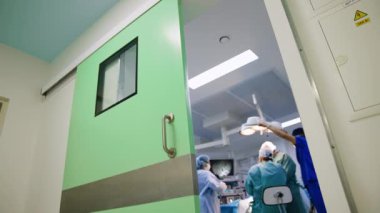 Cerrahi operasyonda açılan kapıdan bakıyorum. Baş cerrah ameliyat masasında oturuyor. Düşük açı görünümü.