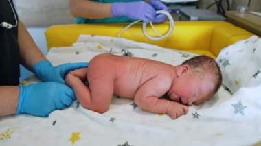 Çıplak yeni doğmuş çocuk karnının üstünde yatıyor. Yenidoğan uzmanı bir bebeğin sağlığını incelemek için steteskop kullanır..