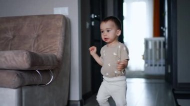 Küçük erkek bebek odaya koştu. Çocuk kamerayı fark eder ve elini uzatır..