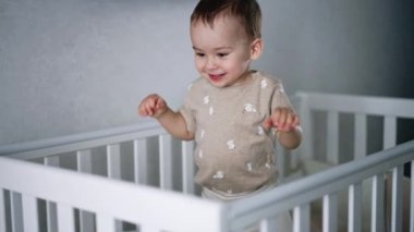 Sevimli çocuk beyaz beşiğinde yürüyor. Oyuncu çocuk yatağı sallamak için zıplar. Evde bebek.