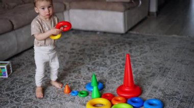 Tatlı bebek piramitten bir yüzük alıyor. Akıllı çocuk oyuncağı odada monte ediyor..