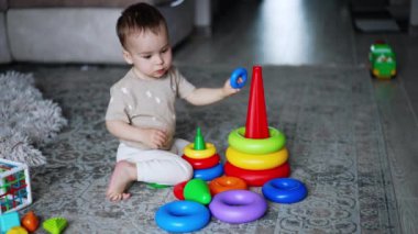 Akıllı küçük çocuk oyuncaklarıyla yerde oynuyor. Piramitleri birleştiren güzel bebek. Yüksek açı görünümü.