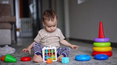 Sevimli küçük çocuk yerde oturan oyuncaklarla oynuyor. Anne oğlunun oyuncağı toplamasına yardım ediyor..