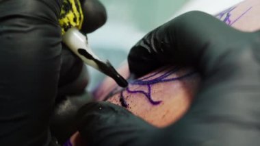 Resmi siyah mürekkeple kaplamak. Siyah eldiven giyen dövmeci işte özel mürekkep makinesi kullanıyor. Kapat..