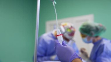 Mavi lateks eldivenleri verin, damlalık deposunu tutun. Ameliyat sırasında takas tezgahını ayarlamak. Cerrahlar arka planda bulanık çalışırlar.