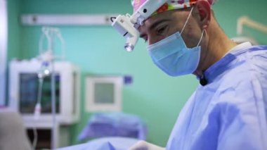 Maskeli bir cerrah, far ve renkli bir şapka. Operasyona odaklanmış bir profesyonelin portresi.