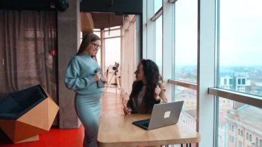 Ofiste iletişim kuran bayan meslektaşlar. İş kadınları laptopta bir şey tartışıyor. Modern ofis arka planda.