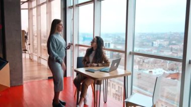 Ofiste fikirler tartışıyoruz. İki bayan meslektaşım aktif ve hareketli konuşuyorlar. Arkaplanda şehir manzaralı panoramik pencere.