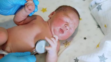 Eldivenli doktor steteskoplu bir bebeği dinliyor. Çıplak bebek el sallıyor. Üst görünüm kapat.