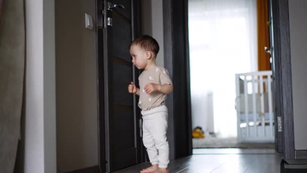 かわいいトッドラーがドアの近くに立っている 子供はドアを押して それがどのように開くかを見ます ローアングルビュー — ストック動画