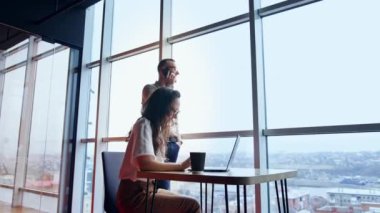 Panoramik pencereli bir ofis ve orada çalışan insanlar. Erkek çalışan telefonda konuşuyor ve kadın dizüstü bilgisayarda çalışıyor. Düşük açı görünümü.
