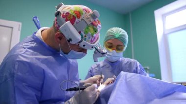 Cerrah göz kapağından ameliyat eder. Doktor aşırı deriden kurtulmak için elektrikli alet kullanıyor. Kadın doktor asistanı..