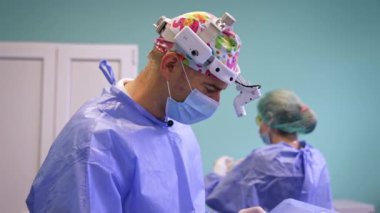Maskeli ve farlı kendinden emin erkek cerrah ameliyathanede çalışıyor. Doktor ameliyat masasındaki hastaya iğne yapıyor..