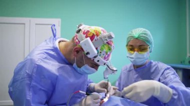 Ameliyat sırasında farlarını değiştiren orta yaşlı bir doktor. Kadın sıhhiyeye yardım etmek alet cihazını bir cerraha geçirir. Göz kapağı estetik ameliyatı.