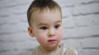 Büyük gri gözleri olan sevimli küçük bebek. Meleklerin beyaz erkek çocuğu bir şeye odaklanmış. Kapat..