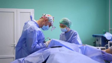 Üniformalı sıhhiyeciler iş başında. Modern hastanede Blepharoplasti. Cerrah, ön far ve elektrikli cihaz kullanıyor..