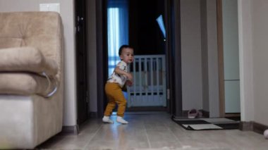 Bebek bir yerden kalkıp koridorda dikiliyor. Gülümseyen mutlu çocuk koşarak odaya koşar..