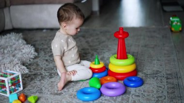 Bir yaşındaki çocuk oyuncak piramitleri söküyor. Küçük erkek bebek evde yerde oynuyor. Yüksek açı görünümü.