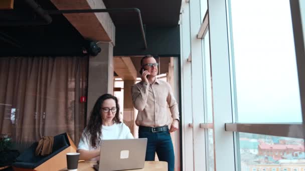 Мужчины Женщины Просторном Офисе Брюнетка Работает Ноутбуком Разговаривает Мужчиной Разговаривающим — стоковое видео