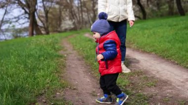 Doğada annesiyle birlikte yürüyen küçük bir çocuk gibi. Kırmızı ceketli bebek yeşil çimlere gider..