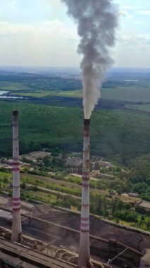 Doğadaki sanayi bölgesi. Dumanlı endüstriyel borular. Yeşil alanlar arasında boruları olan bir metal cerrahi fabrikası. Hava görüntüsü. Dikey video