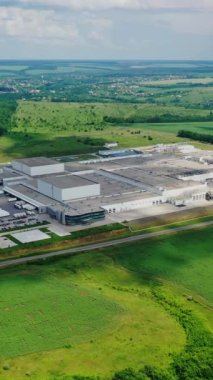 Yeşil doğayla çevrili büyük bir bitki. Yazın kırsal alanda imalat. Modern endüstriyel kompleks sahada. Hava görüntüsü. Dikey video