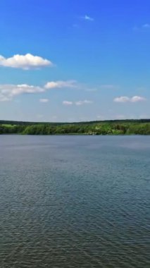 Gündüz vakti mavi nehir. Mavi gökyüzünün altında güzel bir su arka planı var. Yeşil doğa manzarasında geniş bir nehir. Hava görüntüsü. Kamera geri gidiyor. Dikey video