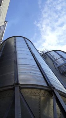 Mavi gökyüzünün altında modern tahıl ambarı. Tahıl depolamak için büyük alüminyum kaplar. Tahıl asansörlerinin dışı. Yakın plan. Aşağıdan bak. Dikey video