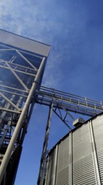 Modern tarım asansörü kompleksi. Mavi gökyüzüne karşı metal ambar. Tahıl işleme için endüstriyel ekipmanlardan yayılan duman. Aşağıdan bak. Dikey video