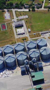 Tahıl asansörleri devrede. Tarım ürünlerini işlemek için fabrikada gümüş silolar. Hasat için modern tahıl ambarına yukarıdan bak. Hava görüntüsü. Dikey video