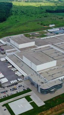 Büyük endüstriyel kompleks. Güzel yeşil yaz manzarasıyla çevrili modern bir fabrika. Sahada park yeri olan büyük bir fabrika. Hava görüntüsü. Dikey video