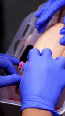 Sonda yerleştirme öğrenimi. Steril eldiven giyen öğrenciler sahte bir ele kateter takmak için çalışıyorlar. Tıbbi eğitim. Yakın plan. Dikey video