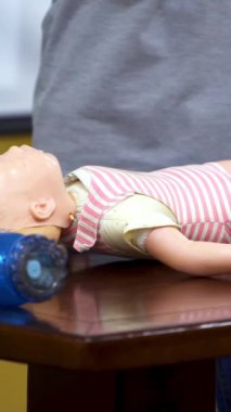İlk yardım eğitimi. Kadın kardiyopulmoner canlandırma eğitimi için kuklayla kalp masajı yapmayı gösteriyor. Manken bebek üzerinde tıbbi bir gösteri. Dikey video