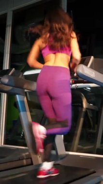Bir spor kulübünde spor yaparken yarış pistinde koşan esmer bir kadının arka görüntüsü. Yeni bir merkez dikey videoda modern bir simülatör üzerinde aktif kadın eğitimi