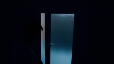 Erkek silueti, aydınlık kapının önündeki karanlık odada hareket ediyor. Karısı bebek doğururken adam endişeleniyor. Üst görünüm.