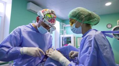 Odaklanmış erkek cerrah cerrahi makas kullanır. Kadın doktor küçük aleti alıp meslektaşına veriyor..