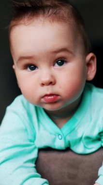 Gri gözlü, saçları yapış yapış bir çocuk ciddi bir yüz ifadesi olan bir sandalyede duruyor. Etrafa bakınan sevimli çocuk. Arkaplan bulanık. Dikey video