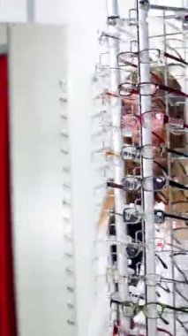 Optik mağazasındaki güzel, uzun saçlı kadın. Yeni gözlükleriyle standın yanındaki şık gözlüklü güzel, gülümseyen genç bayan. Dikey video