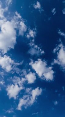 Açık beyaz bulutlar mavi gökyüzü boyunca yayılıyor. Güneş ışınlarında ilahi görünen güzel pamuk bulutları. Zaman ayarlı. Dikey video