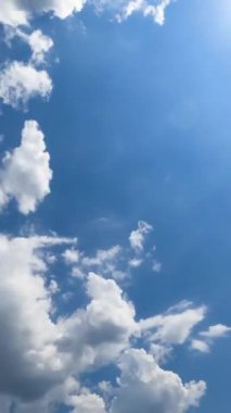Parlak gökyüzünün ışıltılarında hoş kabarık bulutlar. Güzel, güneşli bir günde, alçak açıdan bakıldığında şekil değiştiren bulut manzarası. Zaman ayarlı. Dikey video
