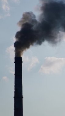 İki fabrika bacası ağır siyah duman üretiyor. Sanayi atmosferi kirletiyor. Bulutlu gökyüzü arka planı. Dikey video
