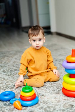 Genç bir çocuk renkli bir yığın bloğun önünde yerde oturuyordu. Sarı bir gömlek ve pantolon giyiyor.