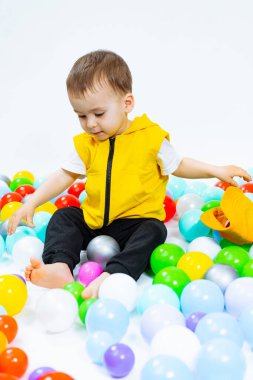 Genç bir çocuk renkli bir top yığınıyla oynuyor. Sahne neşeli ve eğlenceli, çocuk renkli yığının içinde eğleniyor.