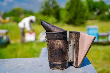 Bir adam bir arı içicisiyle tarlada çalışıyor. Sigara içen yaşlı ve kirlidir. Adam beyaz bir gömlek giyiyor.