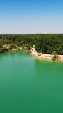 Mavi gökyüzü suya yansıyor. Kalın ormanlarla kaplı olan kıyı şeridine yavaş yavaş yaklaşıyoruz. Hava görüntüsü. Dikey video