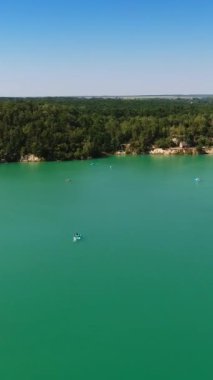 Yeşil ormanlı kayalık kıyılarla çevrili mavi bir gölün güzel manzarası. Mavi gökyüzü suya yansıyor. Hava görüntüsü. Dikey video