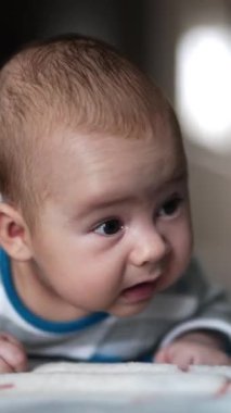 Çizgili tişörtlü bebek başını dik tutmaya çalışıyor. Tombul yanaklı sevimli çocuk. Yaklaş. Arkaplan bulanık. Dikey video